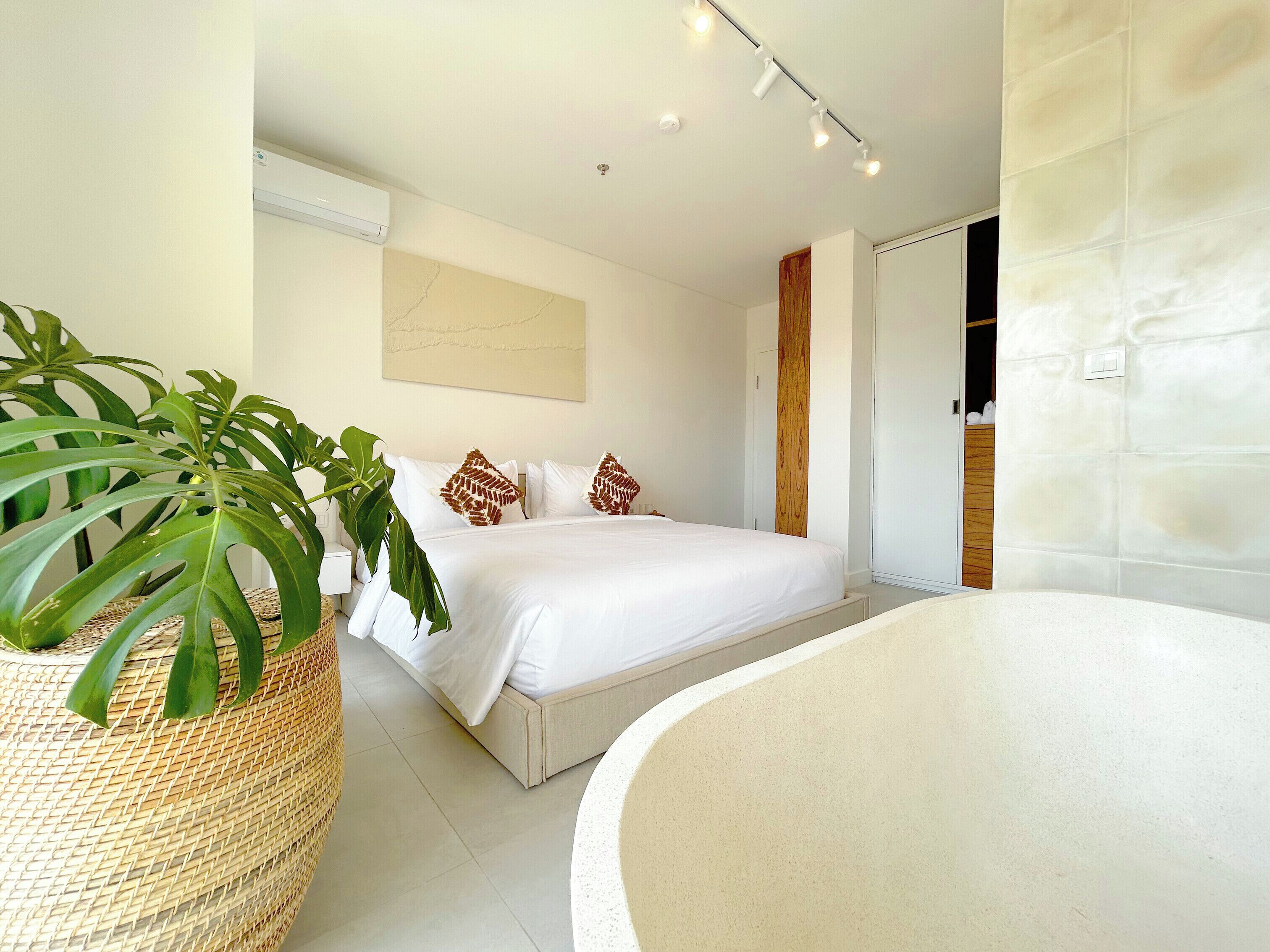 A modern bedroom with a large bed, a bedside plant, and a bathtub.