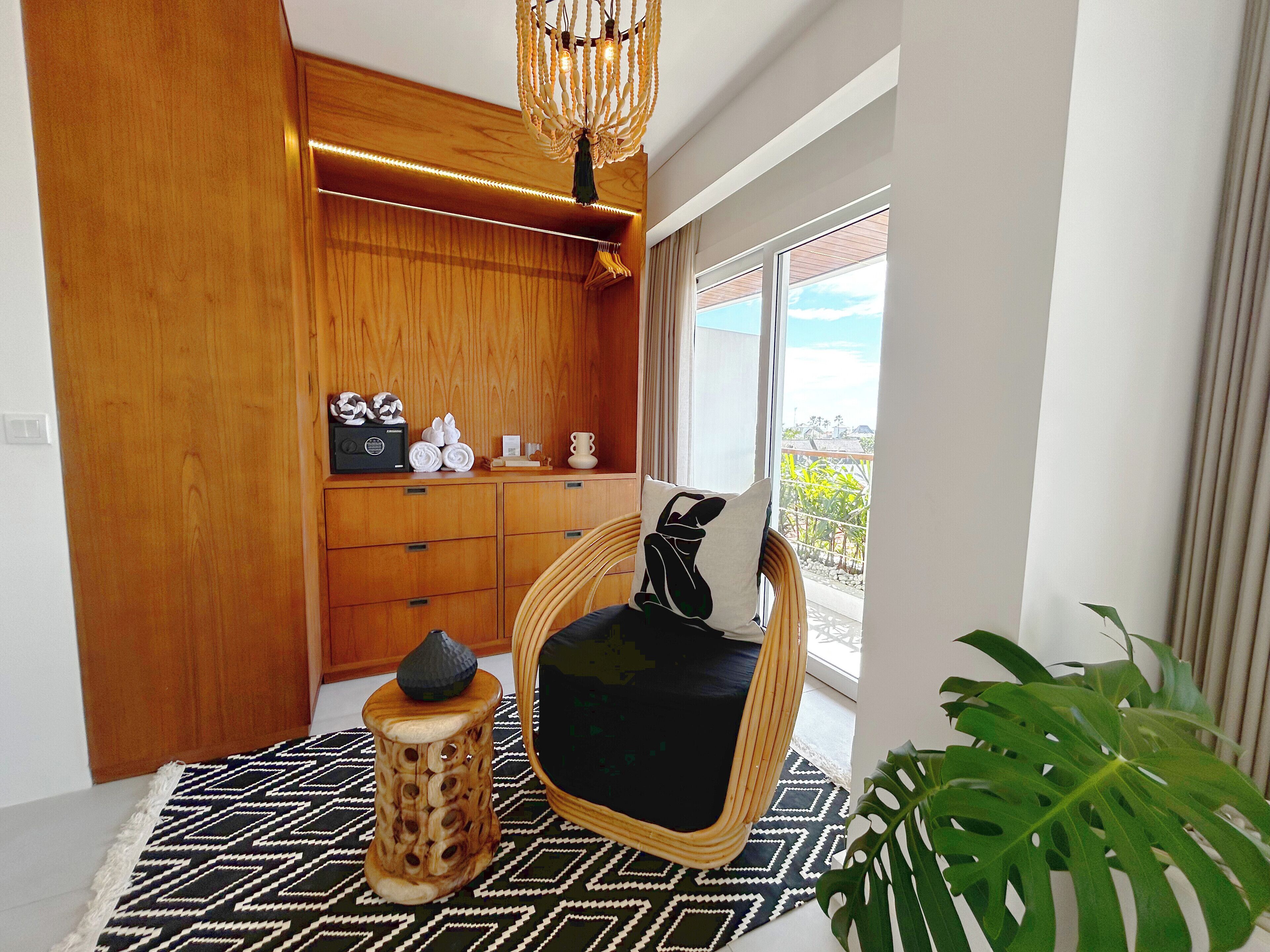 A modern room with a wooden cabinet, a wicker chair with a black cushion, a patterned rug, and a large green plant.