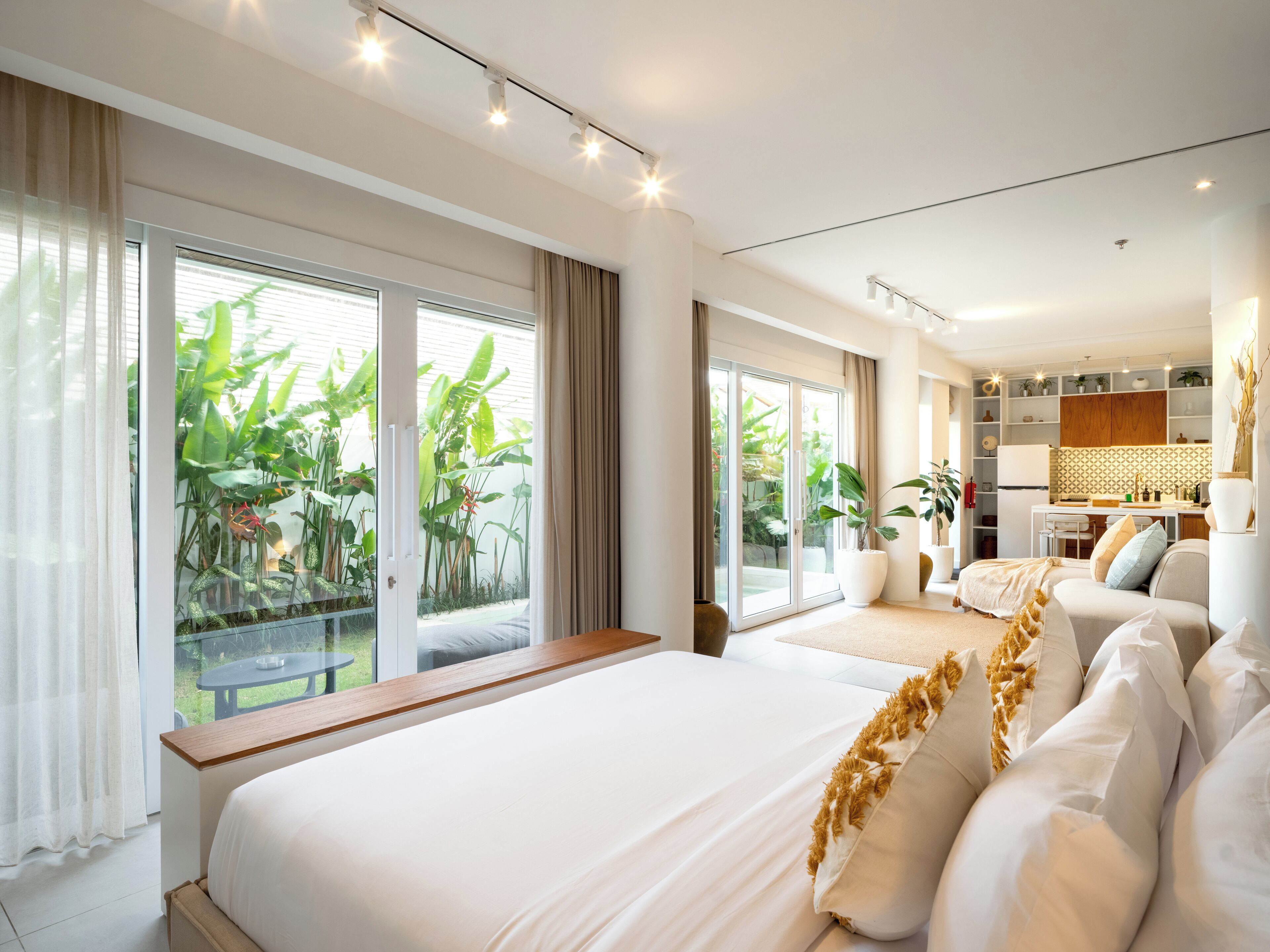 A spacious bedroom with a large bed, a sofa, and a kitchen area visible through an open sliding door.