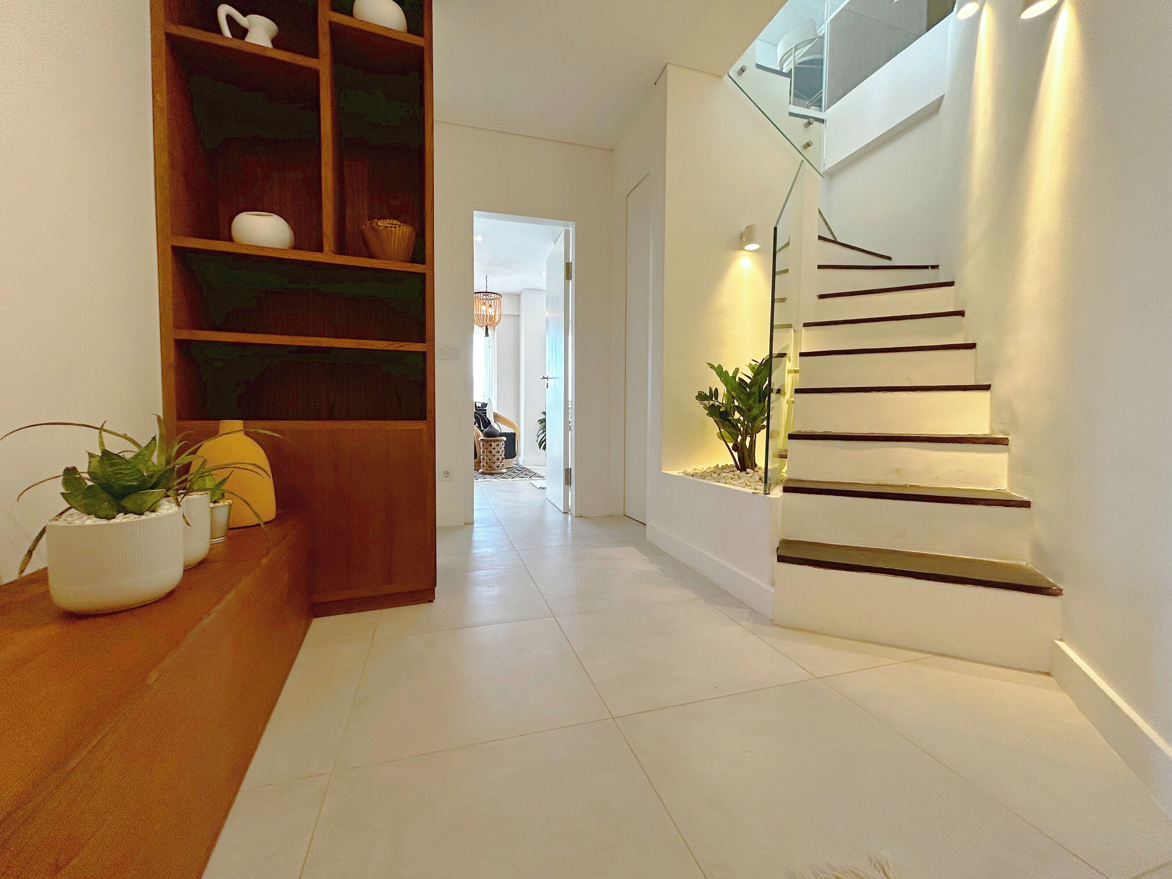 Ein modernes Interieur mit einem Bücherregal aus Holz, einer Treppe mit Glasgeländer und einem Blumentopf.