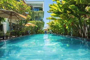 A swimming pool with clear blue water, surrounded by lush greenery and a building with balconies. - Coco Island Villa (Da Nang)