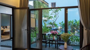 A hotel room with a sliding glass door leading to an outdoor area with a table, chairs, and potted plants. - Coco Island Villa (Da Nang)