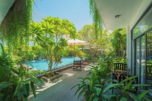 A pool area with a bench and umbrella, surrounded by lush greenery. - Coco Island Villa (Da Nang)