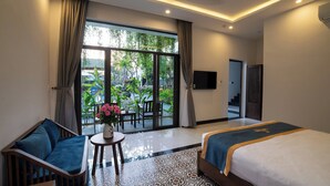 A hotel room with a bed, a sofa, a small table with a vase of flowers, and a large window with curtains. - Coco Island Villa (Da Nang)