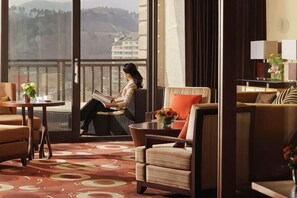 A hotel room with a balcony, a sofa, a chair, a table with a vase, and a view of a cityscape. - Holiday Inn Resort ALPENSIA PYEONGCHANG by IHG (Pyeongchang-gun)