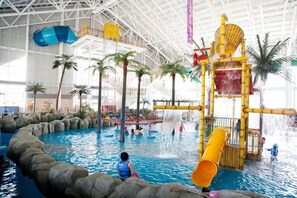 Un parque acuático interior con una piscina grande, toboganes y una estructura de juegos.