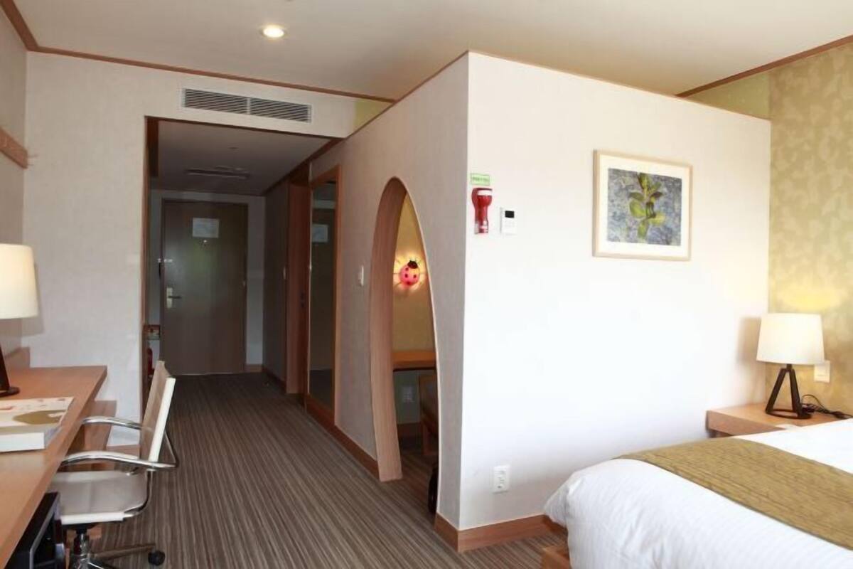 Een hotelkamer met een bed, bureau, stoel en een gang naar een andere kamer.