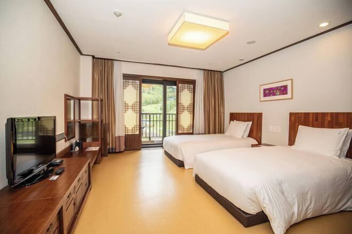 Een hotelkamer met twee bedden, een televisie, een houten dressoir en een glazen schuifdeur naar een balkon.