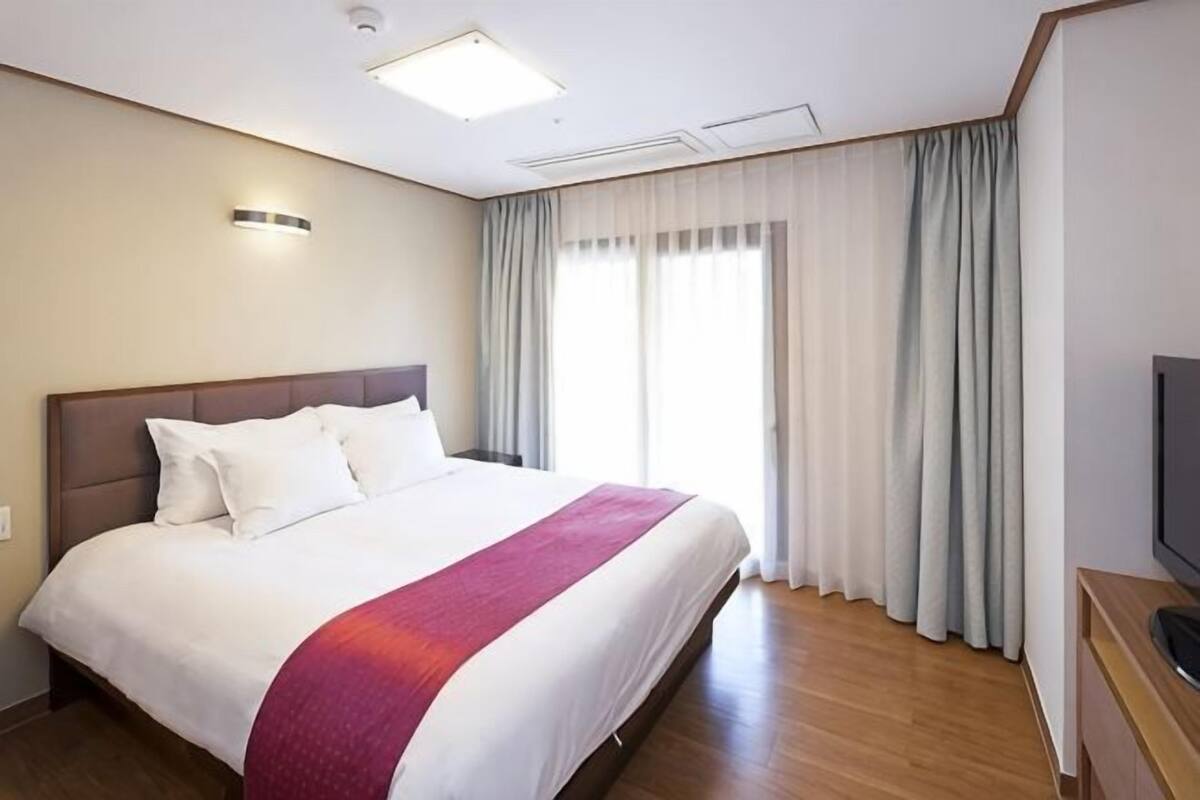 Een hotelkamer met een groot bed, een flatscreen televisie, een raam met gordijnen en een plafondlamp.