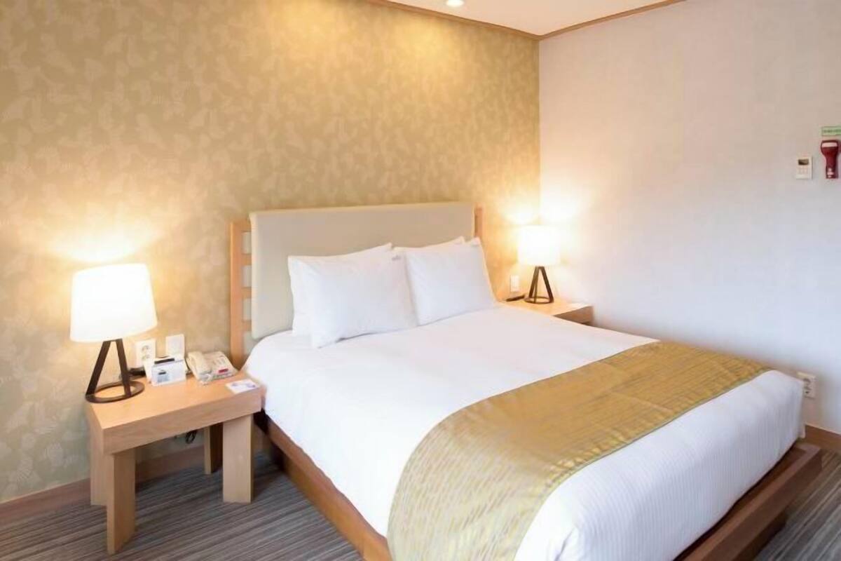 Een hotelkamer met een groot bed, een nachtkastje met een lamp en een aan de muur bevestigd telefoontoestel.