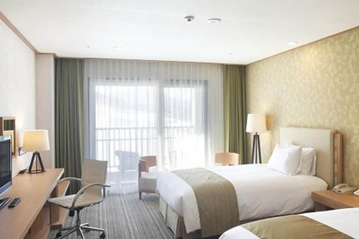 Une chambre d’hôtel avec un lit, un bureau et une chaise, une télévision et une fenêtre avec des rideaux.