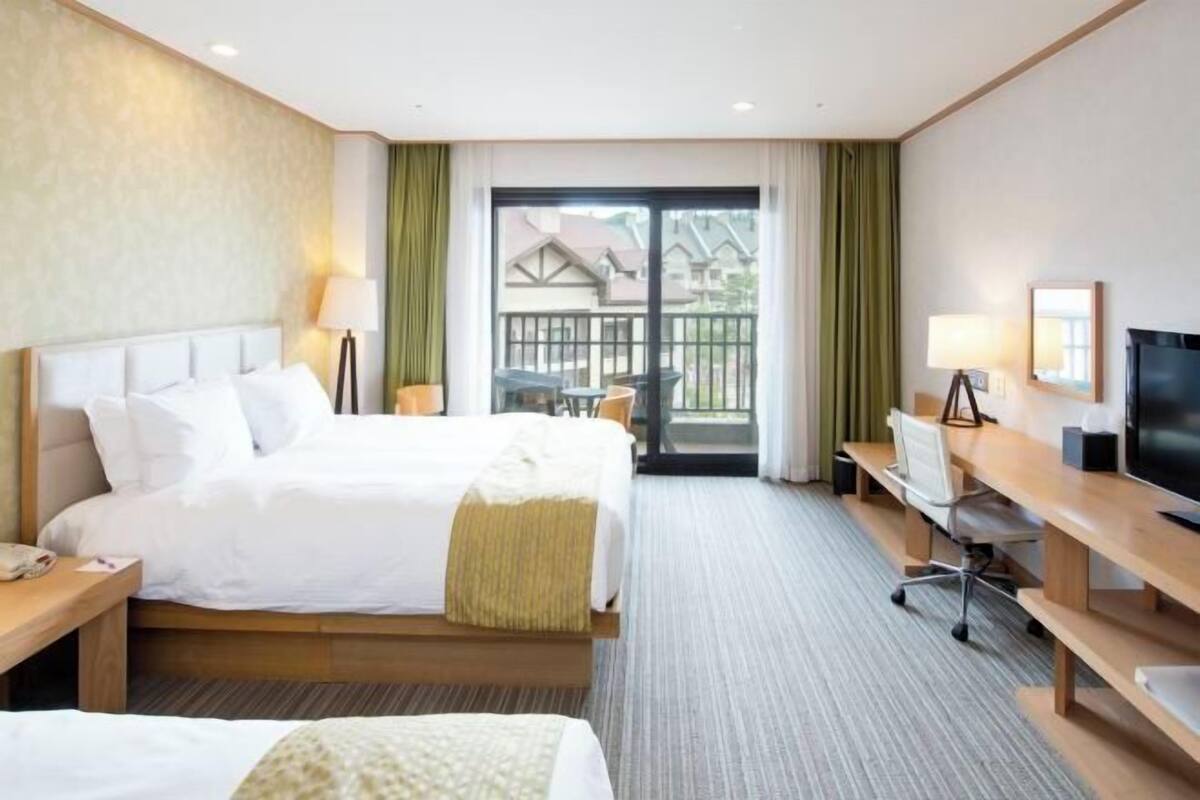 Een hotelkamer met twee bedden, een bureau, een stoel, een televisie en een balkon met uitzicht.