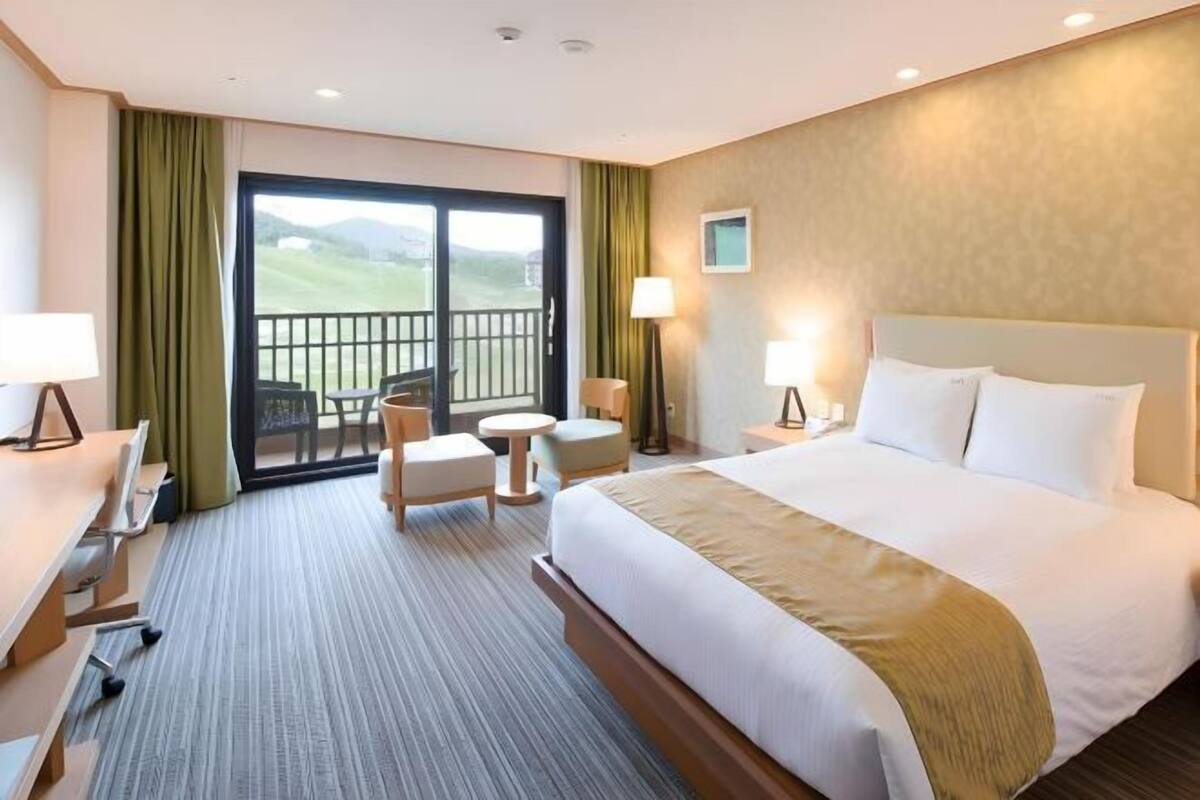 Een hotelkamer met een groot bed, een bureau, een stoel, een kleine tafel en een balkon met uitzicht.