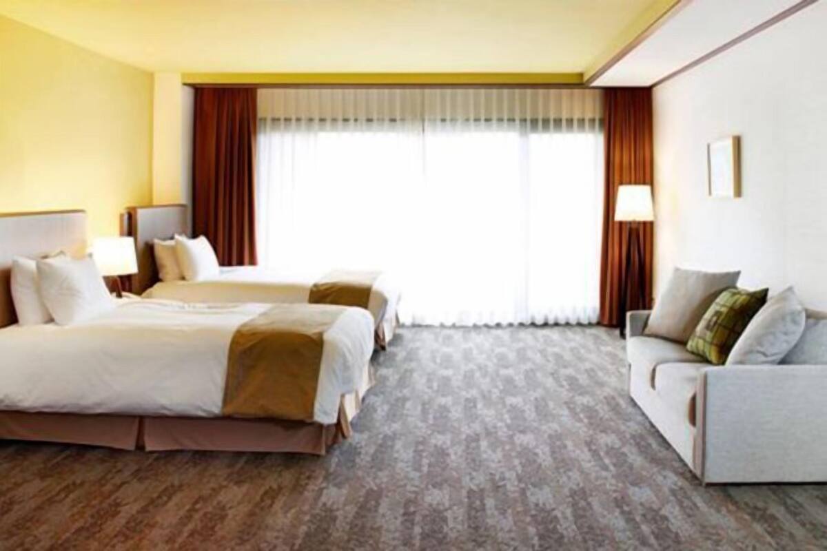 Een hotelkamer met twee bedden, een slaapbank, een lamp en een groot raam met gordijnen.