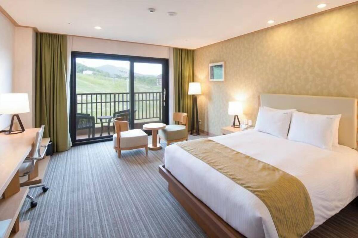 Hotelkamer met een groot bed, een bureau met stoel, een bijzettafeltje en een balkon met uitzicht.