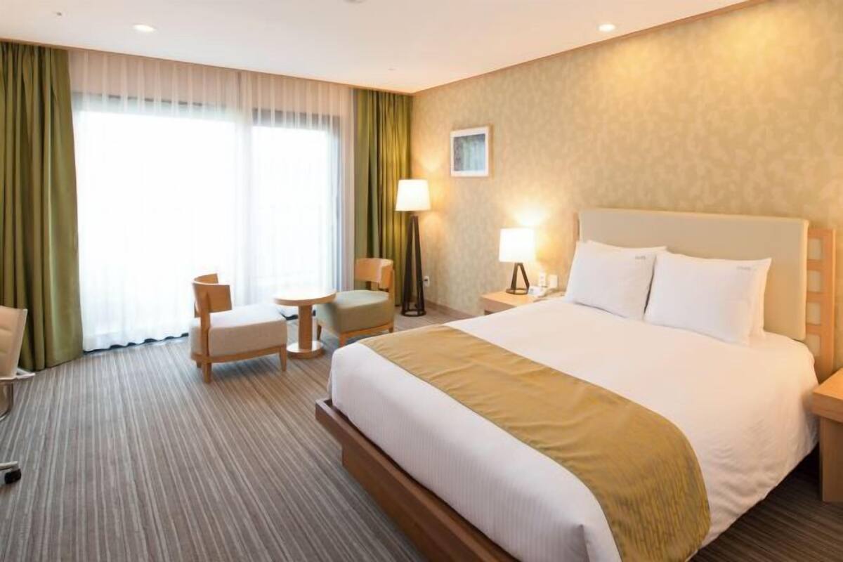 Een hotelkamer met een groot bed, twee nachtkastjes, een bureau, een stoel en een raam met gordijnen.