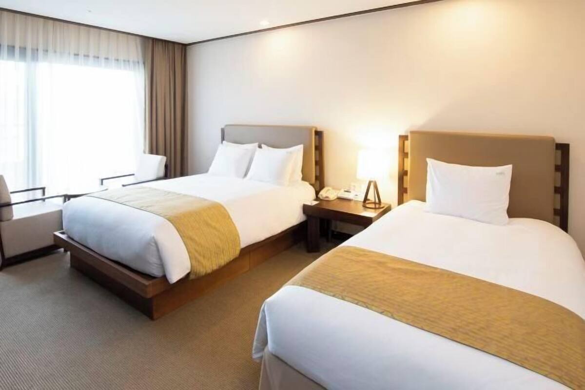 Een hotelkamer met twee bedden, een bureau, een stoel en een raam met gordijnen.