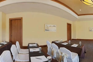 Un salón de conferencias con una larga mesa, sillas blancas y un cuadro en la pared.
