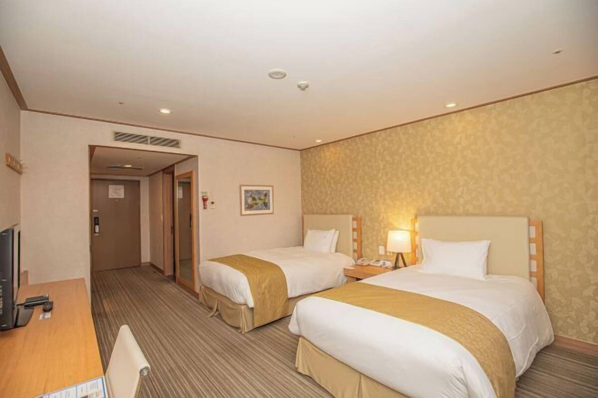Een hotelkamer met twee bedden, een bureau met een stoel, een televisie en een deur naar een andere kamer.