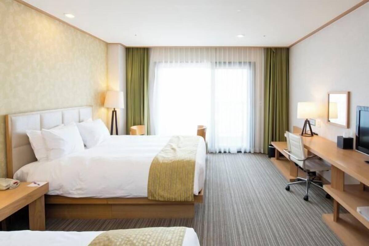 Een hotelkamer met twee bedden, een bureau, een stoel, een televisie en een raam met gordijnen.