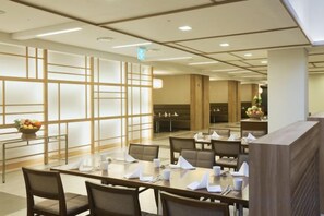 Une salle à manger d’hôtel comprenant plusieurs tables, des chaises et un mur décoratif orné d’un motif géométrique.