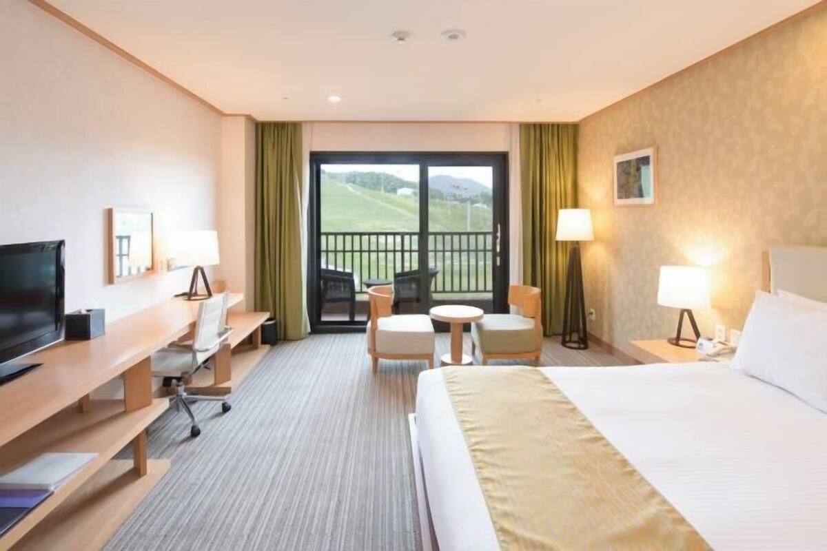 Hotelkamer met een bed, bureau, televisie, stoelen en een balkon met uitzicht.