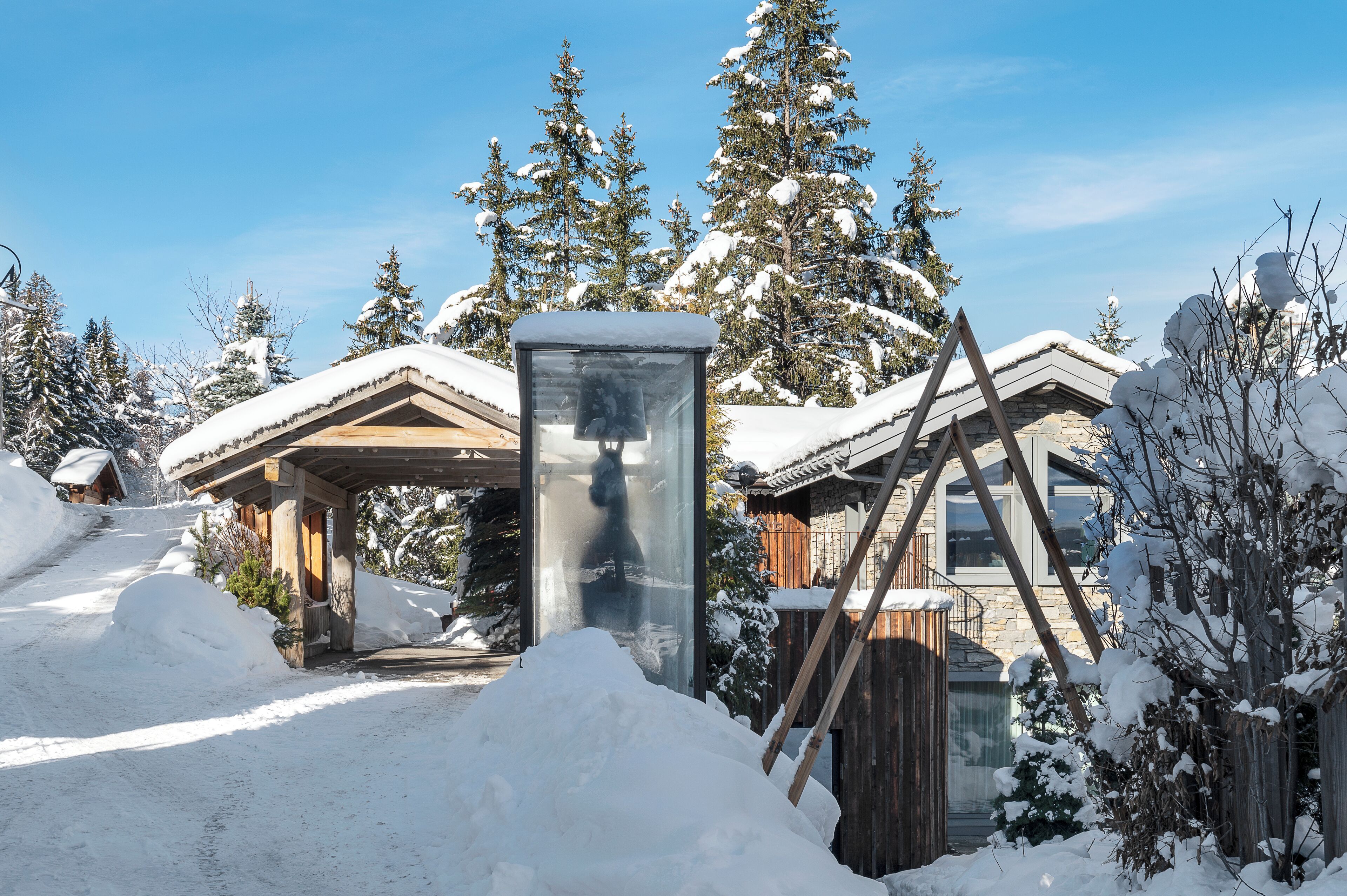 Un chalet enneigé doté d’une structure en verre, de poutres en bois et entouré d’arbres chargés de neige.