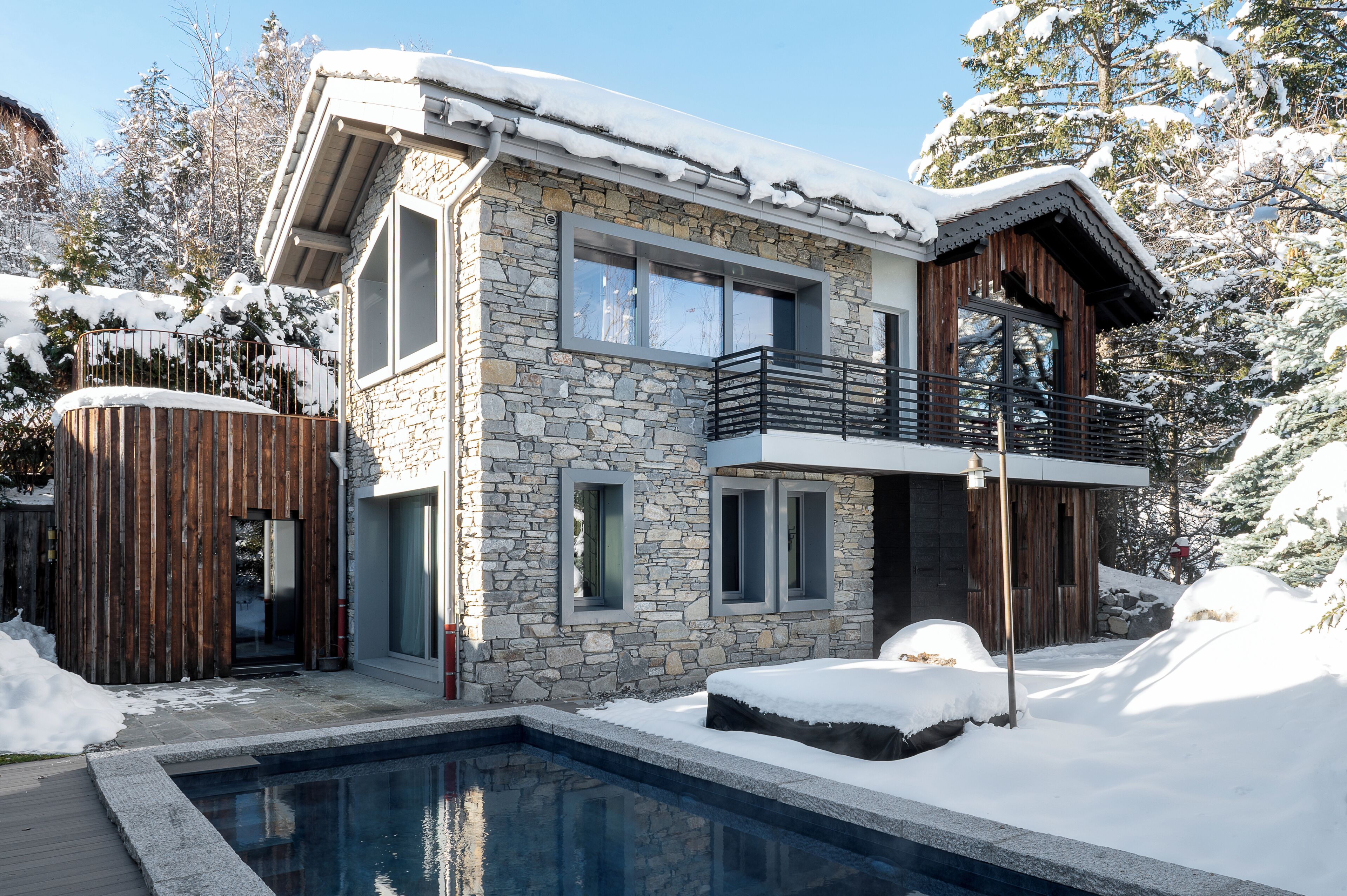 A modern two-story house with a stone facade, a wooden deck, and a swimming pool.