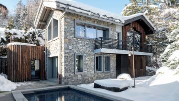 A modern two-story house with a stone facade, a wooden deck, and a swimming pool.