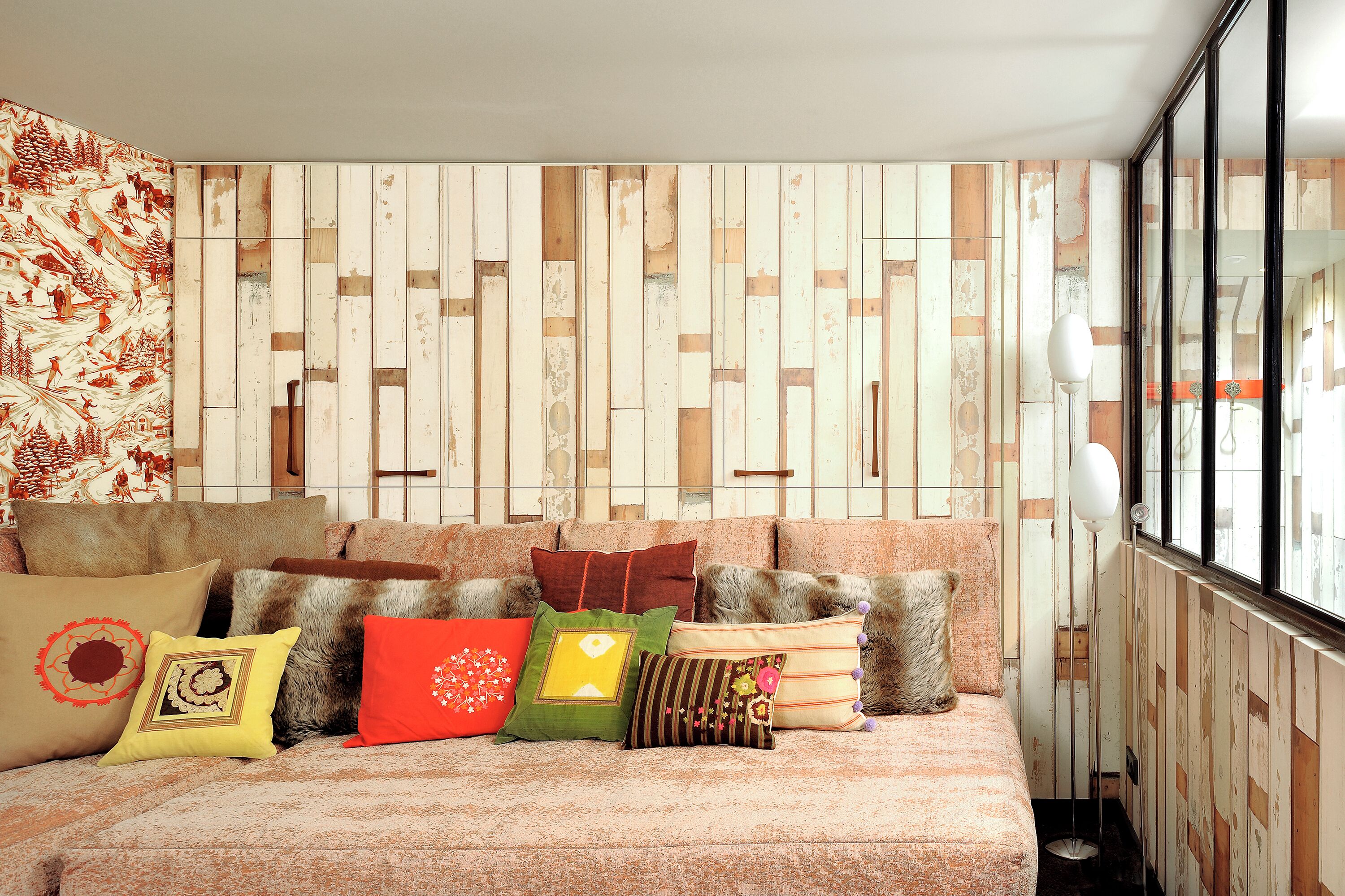 Una habitación acogedora con un papel tapiz estampado, un sofá mullido con varios cojines y una lámpara de pie alta.