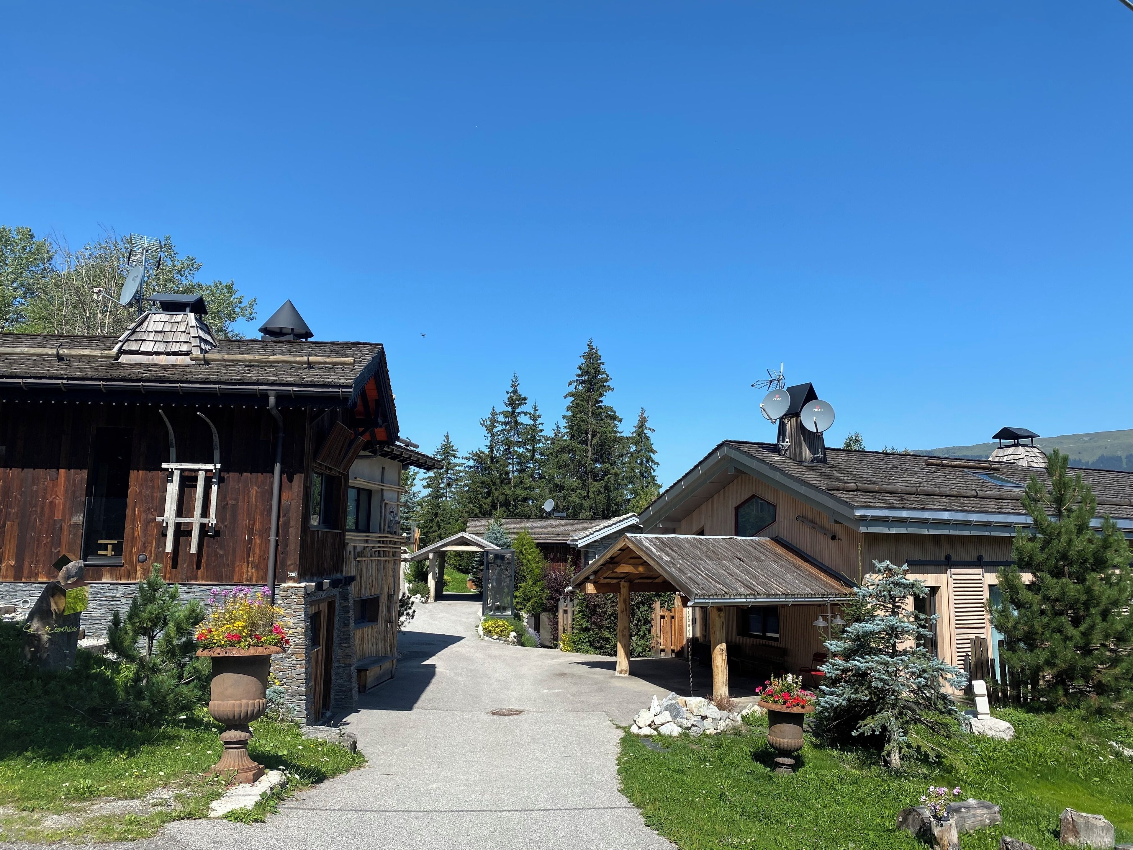 A rustic wooden building with a stone entrance, a wooden porch, and a clear pathway leading to a gate.