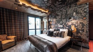 A bedroom with a large bed, a wooden bench, a plaid curtain, and a floral wallpaper. - Le Hameau de Marcandou (Courchevel)