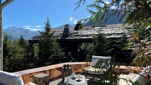 A wooden deck with a stone fireplace, outdoor seating, and a view of mountains. - Le Hameau de Marcandou (Courchevel)