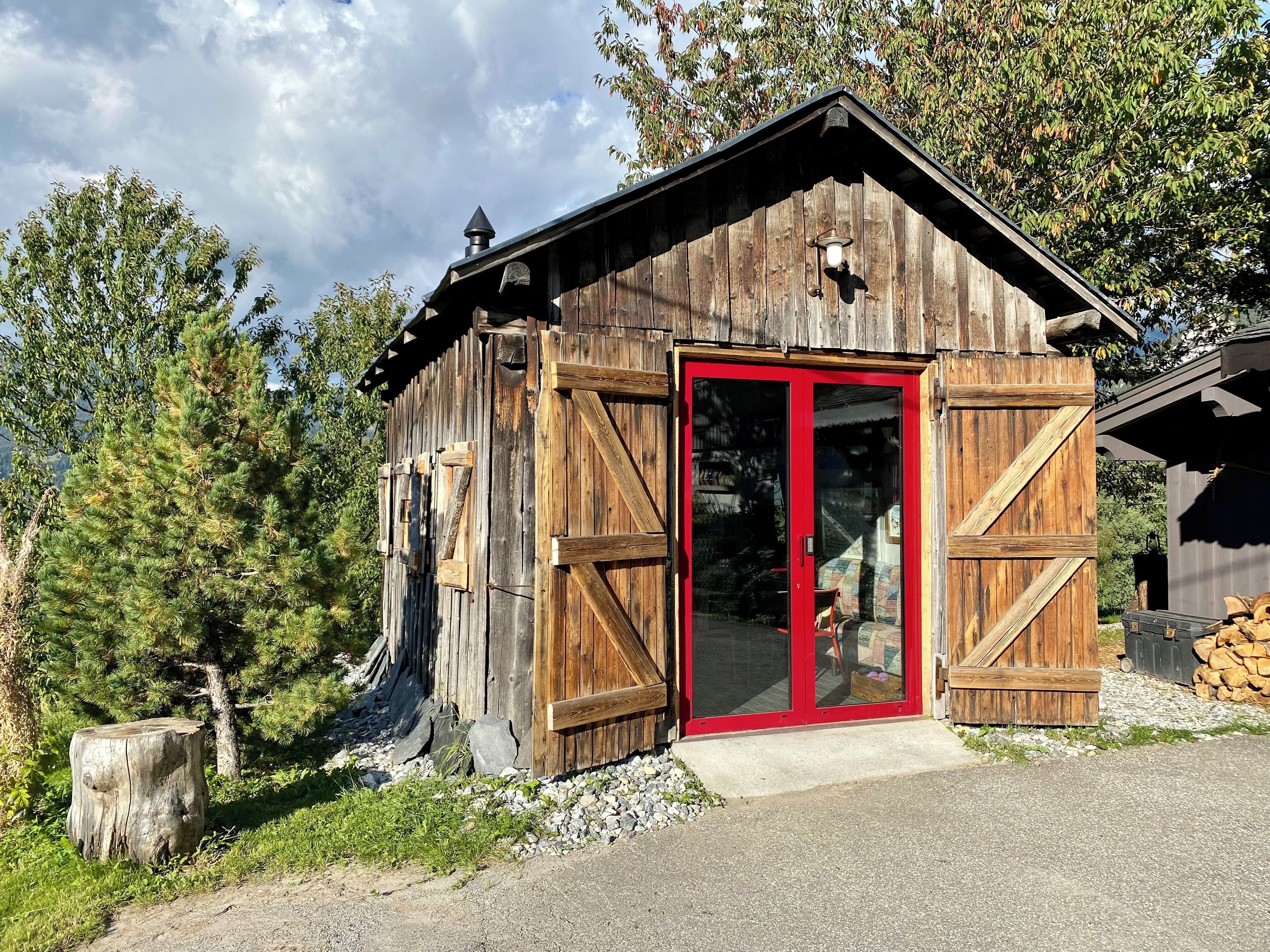Una cabaña rústica de madera con puerta roja, ventanas grandes y chimenea.