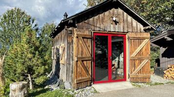 Una cabaña rústica de madera con puerta roja, ventanas grandes y chimenea.