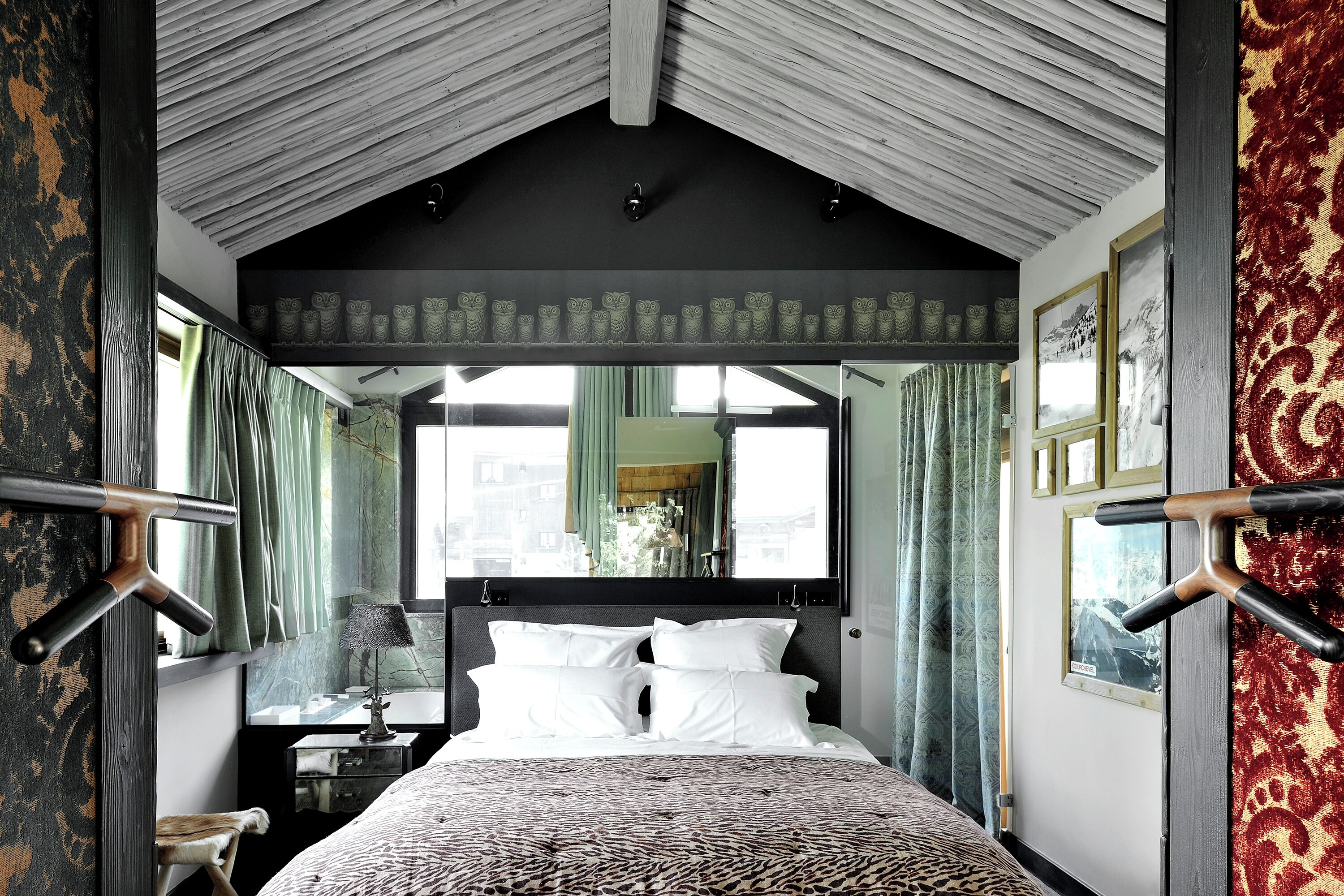 A bedroom with a large bed, a nightstand, a mirror, and a window with curtains.