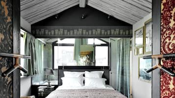 A bedroom with a large bed, a nightstand, a mirror, and a window with curtains.