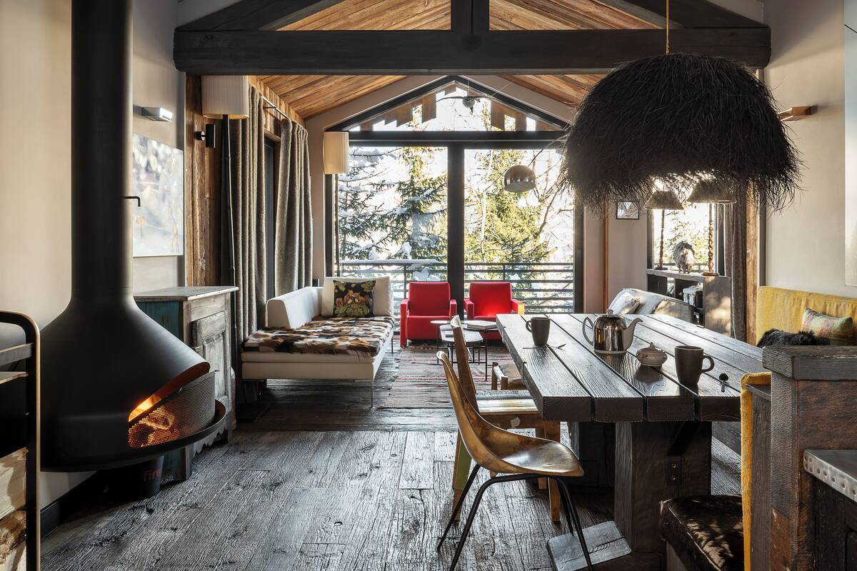 Interior acogedor de una cabaña con estufa de leña, una mesa de comedor y un sofá.