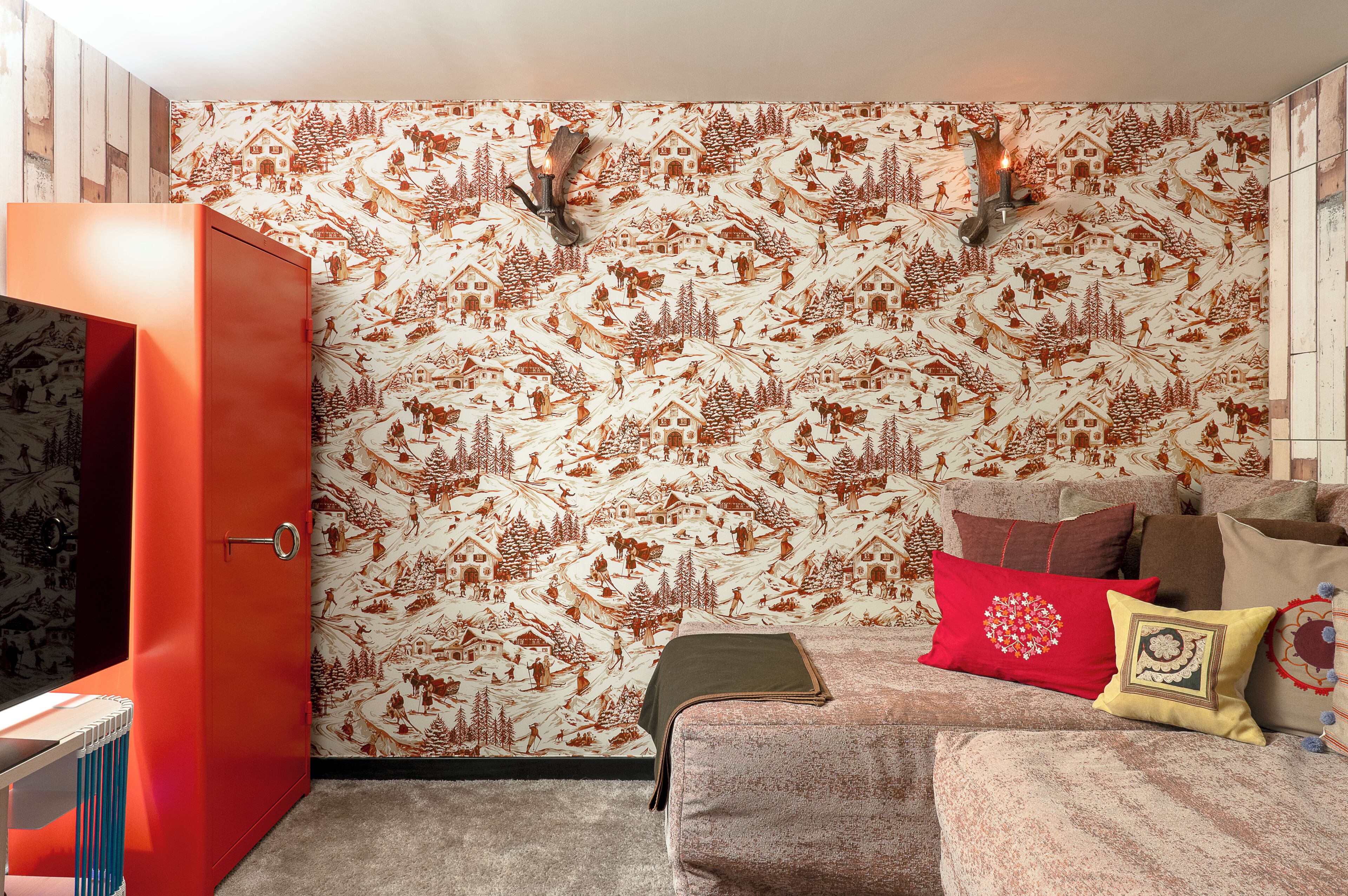 A room with a patterned wallpaper, a red cabinet, and a sofa with multiple cushions.