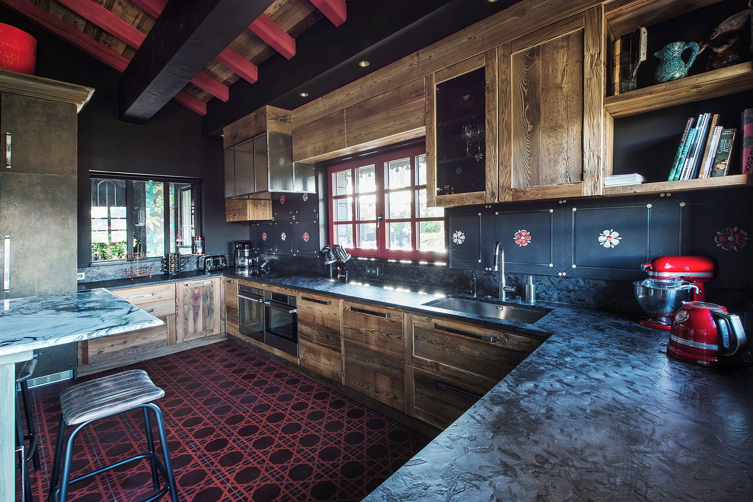 A modern kitchen with wooden cabinets, a red patterned floor, and a large window.