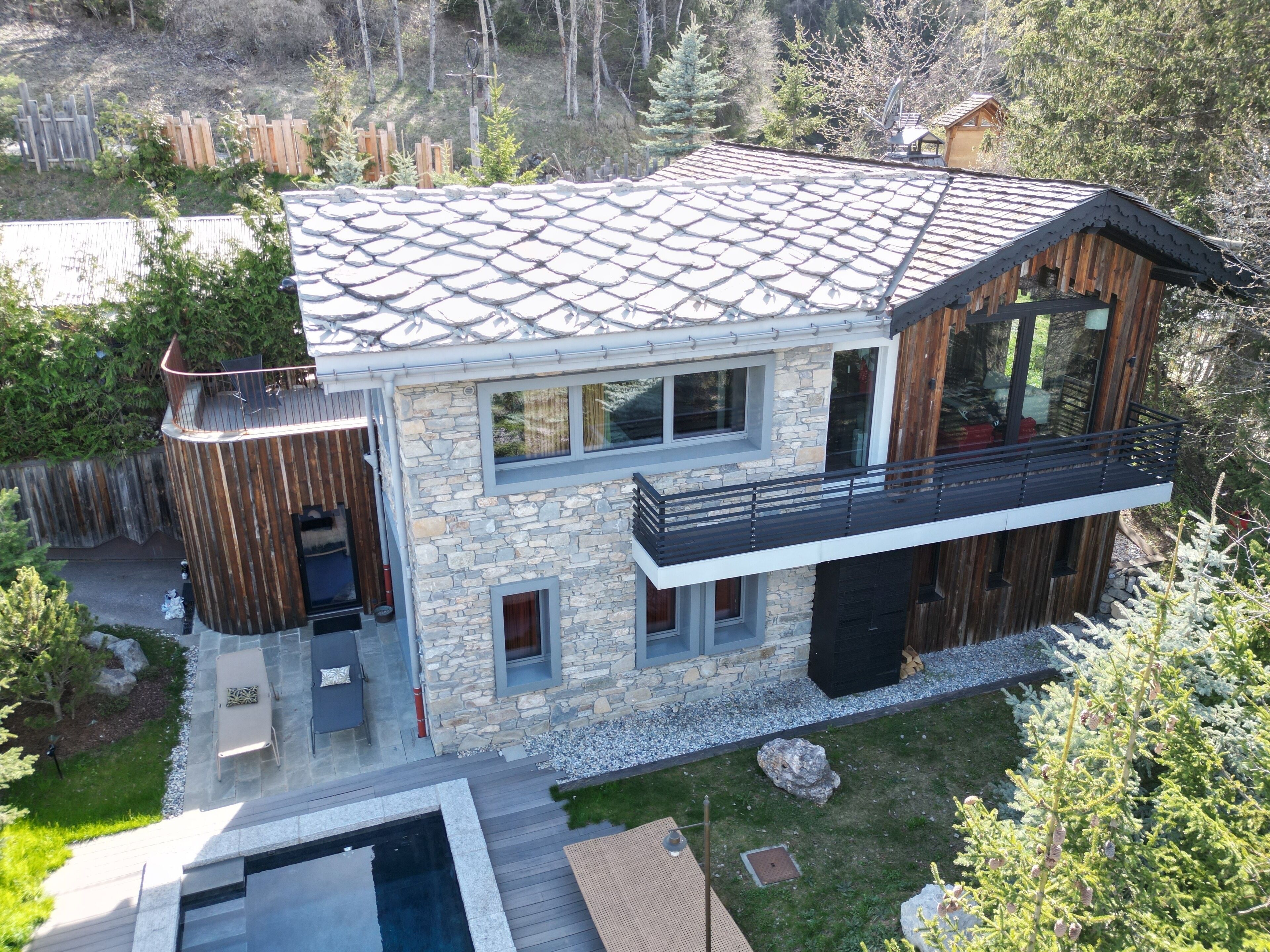 Una casa moderna de dos pisos con fachada de piedra, un balcón y una piscina.