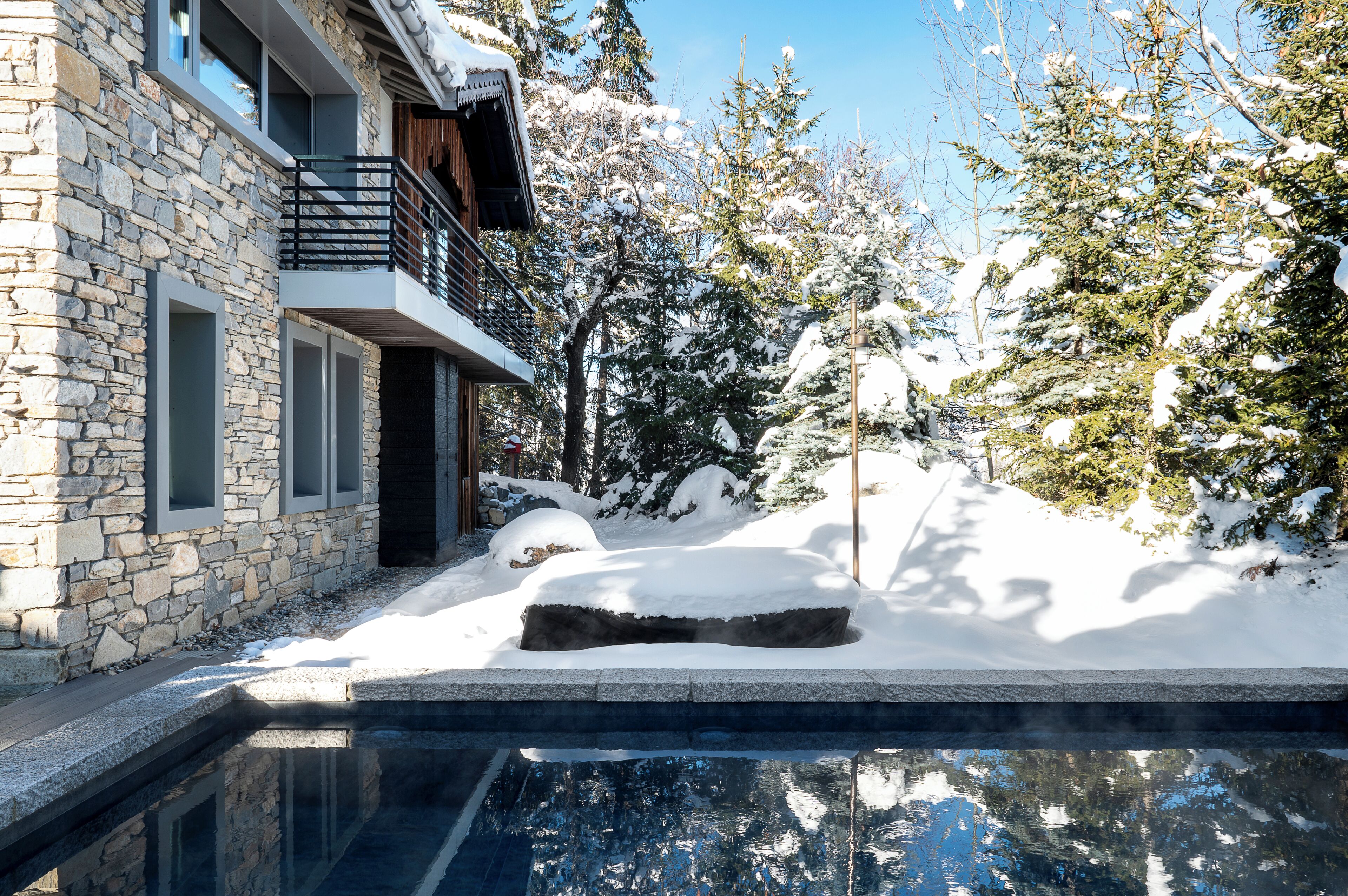 A stone building with a balcony, a snow-covered landscape, and a swimming pool.