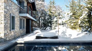 A stone building with a balcony, a snow-covered landscape, and a swimming pool.