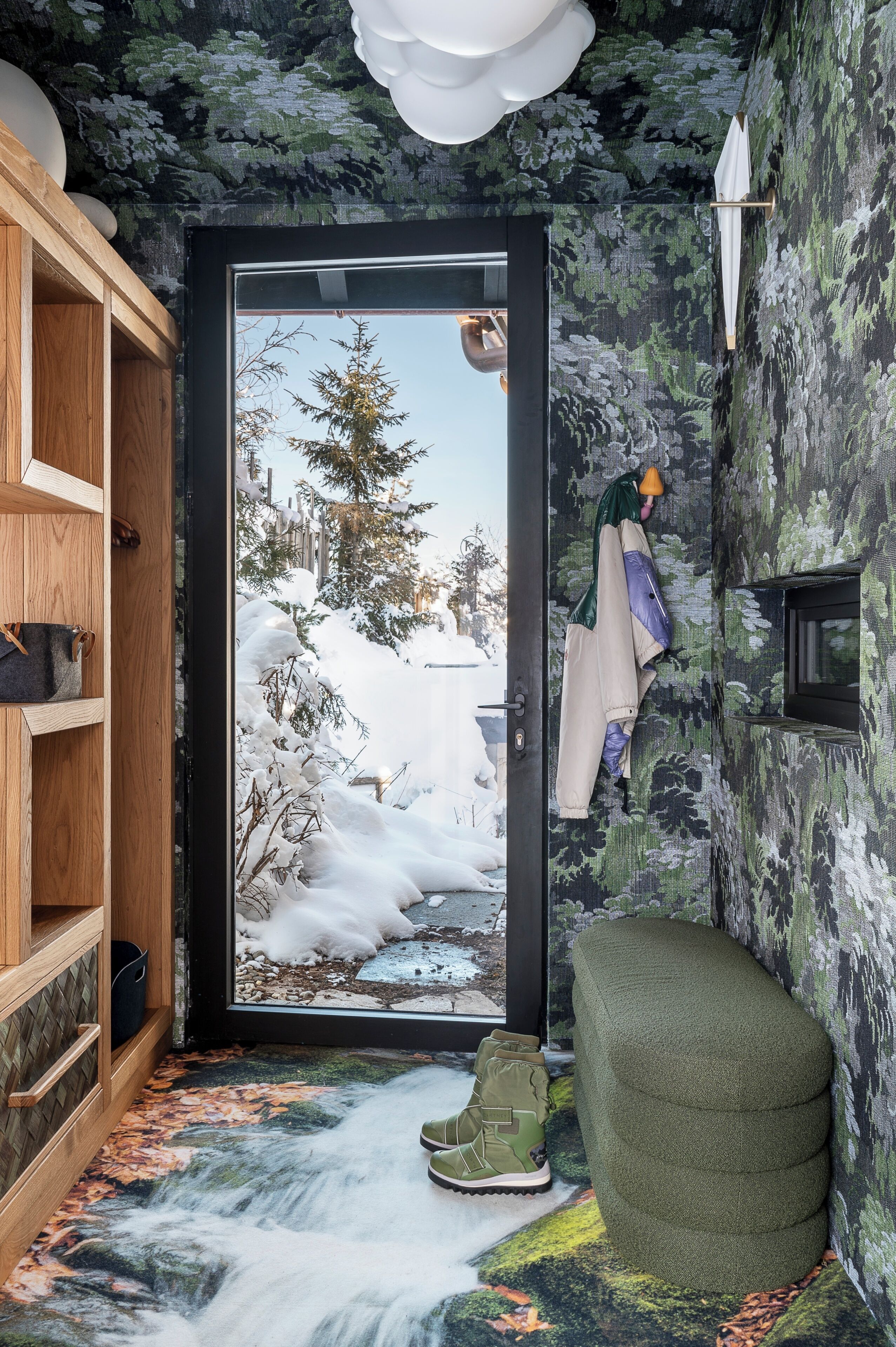 A room with a door leading to a snowy outdoor scene, a wooden shelf, a green ottoman, and a pair of green boots.