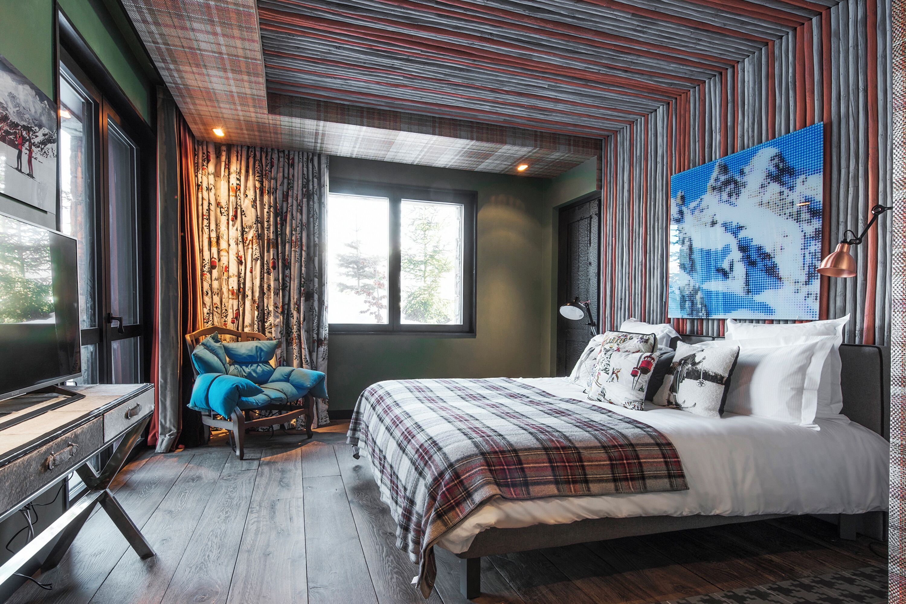 A bedroom with a bed, a chair, a desk, and a large window.