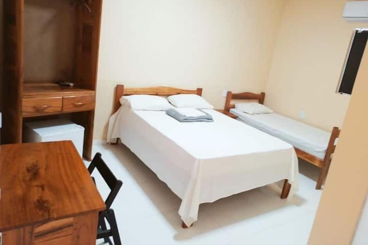 A small, single-room accommodation with a wooden desk, two single beds, and a wardrobe.