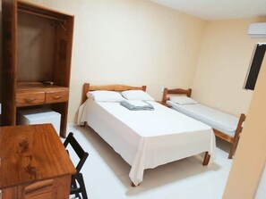 A small, single-room accommodation with a wooden desk, two single beds, and a wardrobe.