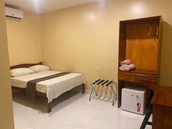 Una habitación con cama, un armario de madera, un refrigerador pequeño y un radiador.