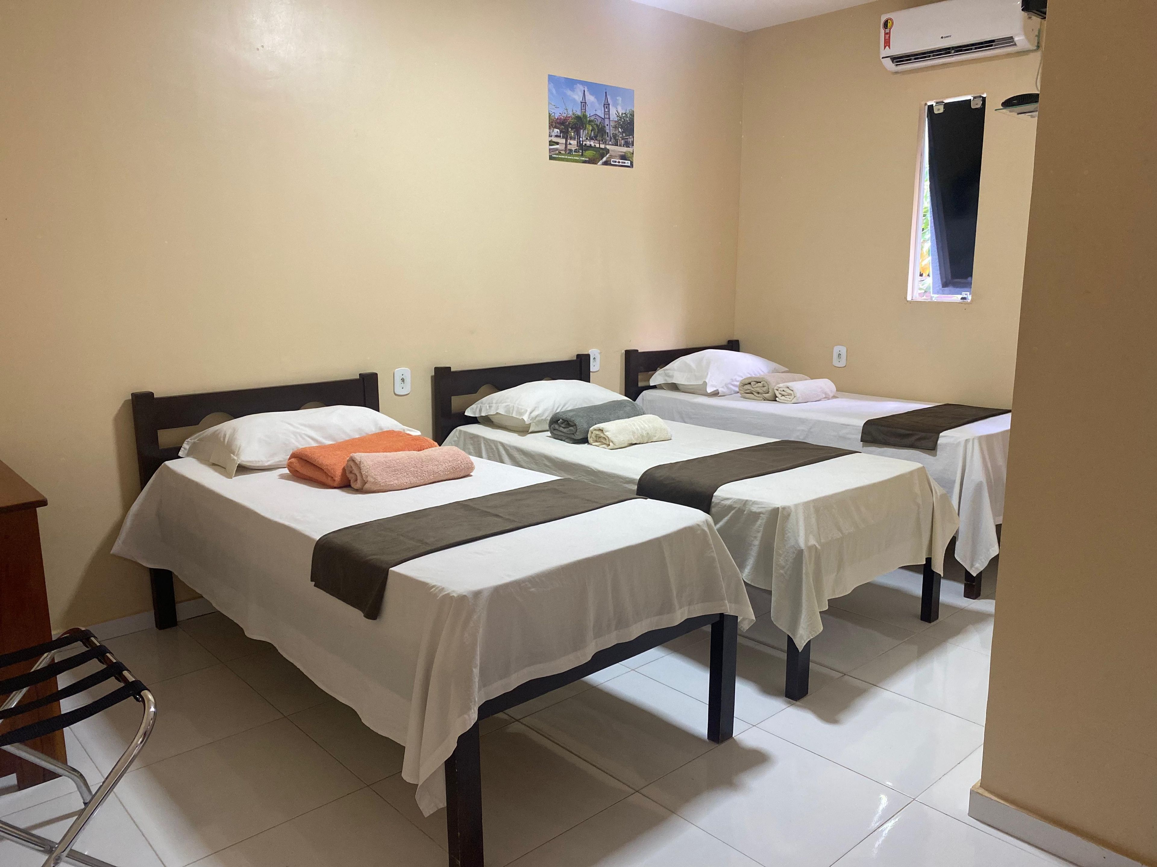 Habitación de hotel con tres camas individuales, un escritorio y un equipo de aire acondicionado.