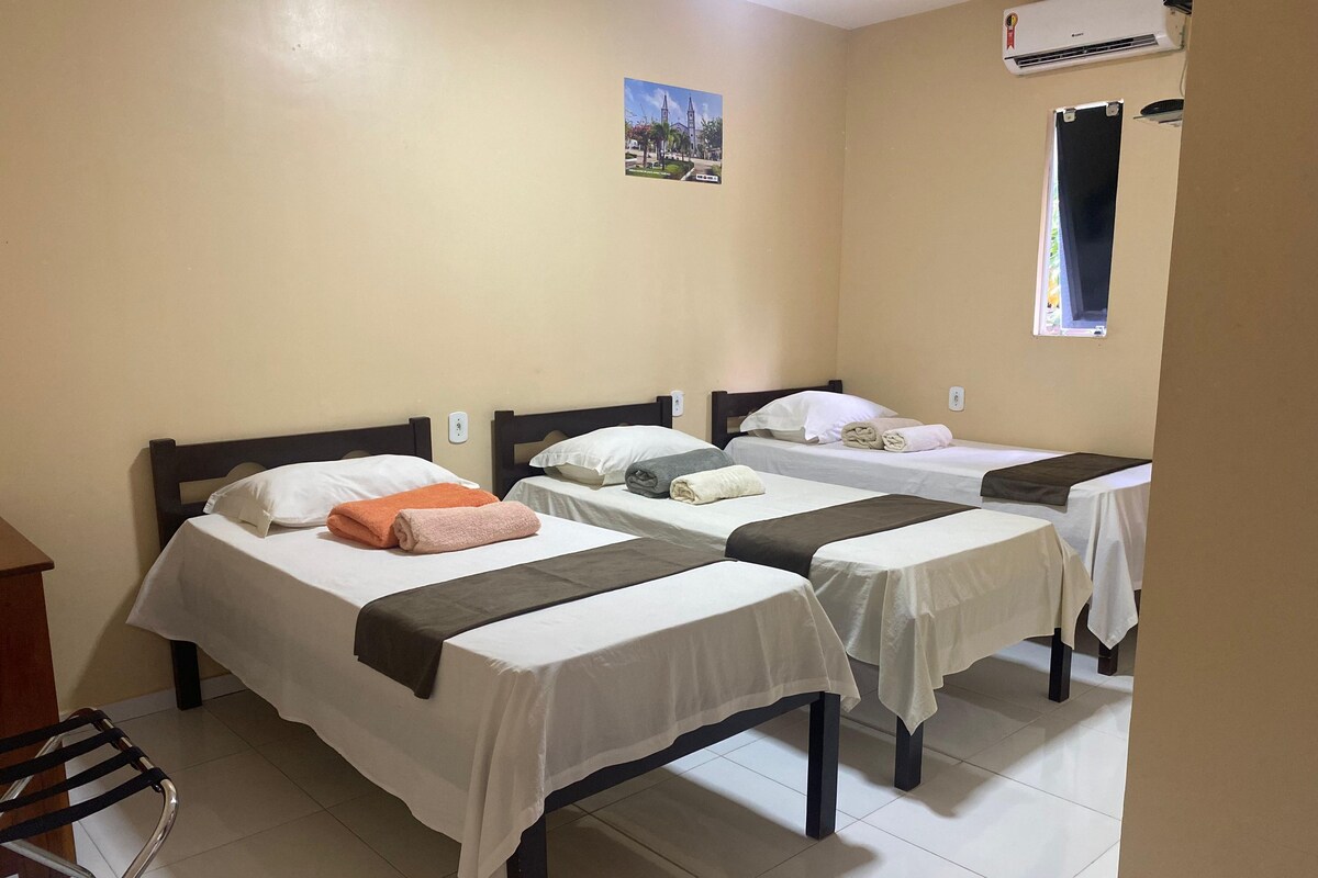 A hotel room with three single beds, a desk, and an air conditioning unit.